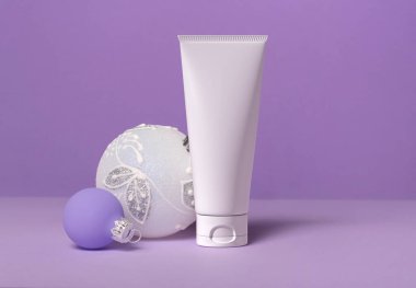 White tube of cream on a lilac background with Christmas balls