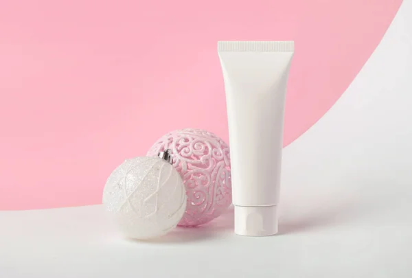 White tube of cream on a pink background with Christmas balls