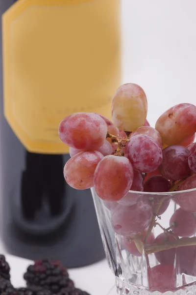 Бутылка красного вина и бокал, наполненный виноградом — стоковое фото