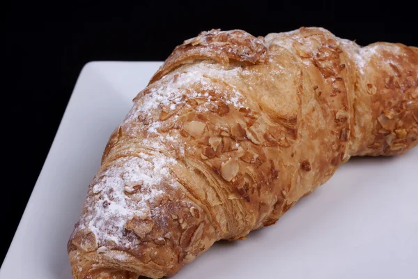 Croissant de amêndoa fresca em um fundo preto — Fotografia de Stock