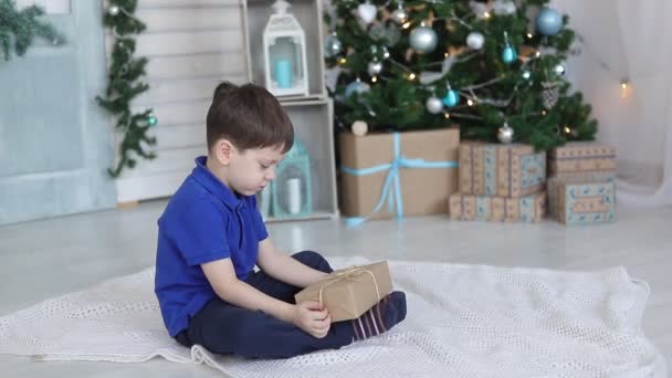 Um rapaz com um presente debaixo da árvore de Natal. Humor festivo. Um presente para o ano novo. Ano Novo e Natal. — Vídeo de Stock