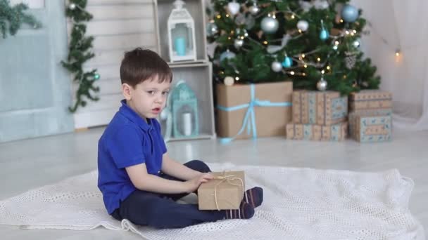 Un ragazzo con un regalo sotto l'albero di Natale. L'umore festivo. Un regalo per il nuovo anno. Capodanno e Natale. — Video Stock