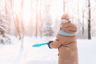 Çocuk kürekle kar fırlatıyor. Kış yürüyüşleri. Çocukların kış tatili hakkında bir makale. Eğlenceler