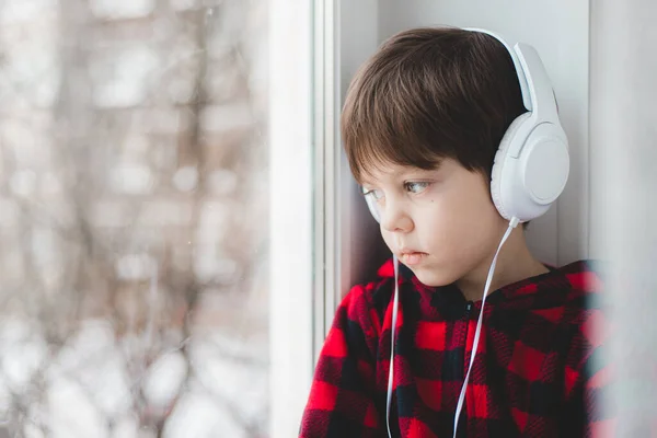 A boy with headphones looks out the window . Modern children. Social media. An article about modern children. — Zdjęcie stockowe