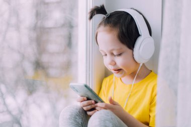 A boy with a phone is sitting on a lifestyle window . Social media. Modern children. An article about developed children.