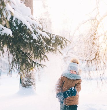 A boy shakes a snow-covered branch of a lifestyle spruce. Winter painting. Winter walks. Happy childhood .
