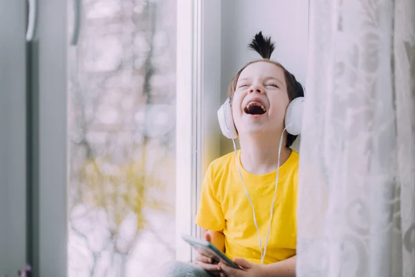 A boy with a phone is sitting on a lifestyle window . Social media. Modern children. An article about developed children. — Zdjęcie stockowe