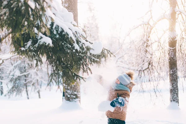 A boy shakes a snow-covered branch of a lifestyle spruce. Winter painting. Winter walks. Happy childhood . — Photo