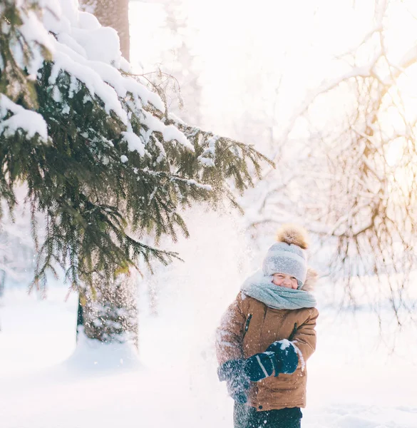 A boy shakes a snow-covered branch of a lifestyle spruce. Winter painting. Winter walks. Happy childhood . — Photo