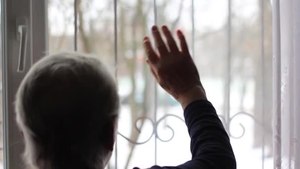Ηλικιωμένη γυναίκα, η γιαγιά κουνάει το χέρι της από το παράθυρο. — Αρχείο Βίντεο