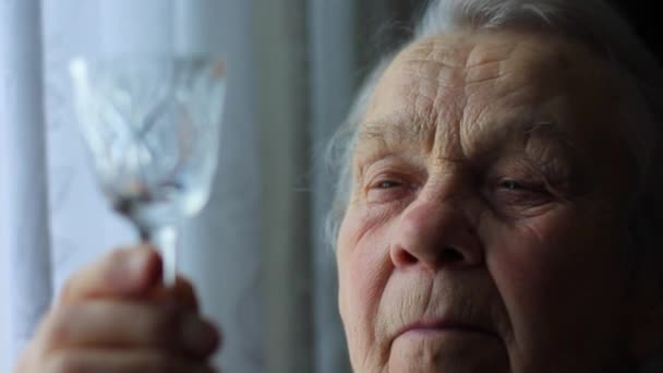 Una anciana, una abuela, sostiene un vaso en sus manos y lo examina. — Vídeos de Stock