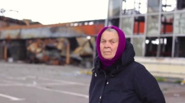 Yaşlı kadın, büyükanne, yıkılmış bir binanın arka planında tek başına..