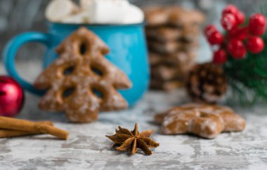 Yıldız anason, tarçınlı çubuk, lezzetli zencefilli ekmek, yeni yıl dekorasyonu ve mavi bir bardak çikolatalı içecek.