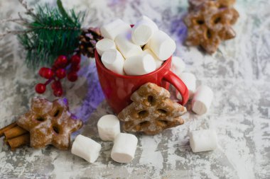 Kokulu zencefilli kurabiyeler, kırmızı bardakta çiğneyen beyaz marşmelov ve açık arkaplan manzaralı yeni yıl dekoru..