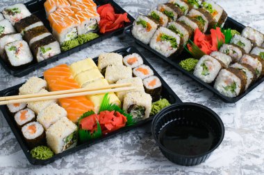 Hafif arkaplanlı plastik ambalajda wasabi ve soya soslu birkaç set suşi. Lezzetli rulo karides, salatalık, havuç ve ıspanak. Evinize ya da ofisinize yemek teslimatı