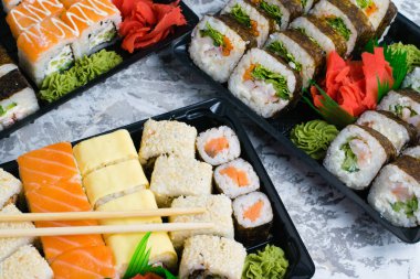 Hafif arkaplanlı plastik ambalajda wasabi ve soya soslu birkaç set suşi. Lezzetli rulo karides, salatalık, havuç ve ıspanak. Evinize ya da ofisinize yemek teslimatı