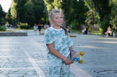 Yaz günü şehir parkında kaykaylı gülümseyen bir genç..