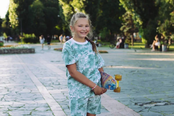 Güneşli bir yaz gününde parkta kaykaylı tatlı gülümseyen genç kız eğleniyor. Gençler ve tatildeki çocuklar için sağlıklı yaşam tarzı kavramı.