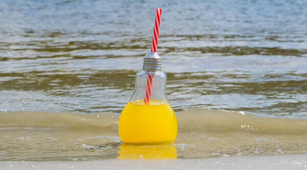 Fresh, lemonade or cocktail in a glass bottle with a straw close-up on the beach sand near the water. Travel and recreation concept