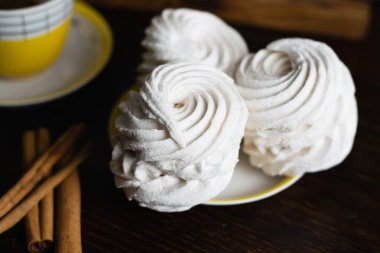 Aromatik marşmelov ve çay tabağında tarçın ve koyu arkaplanda klasik sarı bir fincanda kahve..