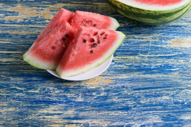 Beyaz bir tabakta olgun karpuz dilimleri ve arka planda yarım karpuz. Yaz tatili konsepti ve uygun beslenme.