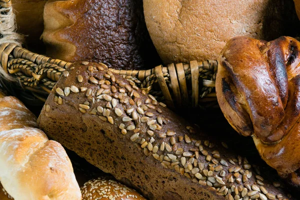 Ассортимент хлеба крупным планом. Сладкая булочка, багет, длинный хлеб, белый и черный хлеб в корзине — стоковое фото