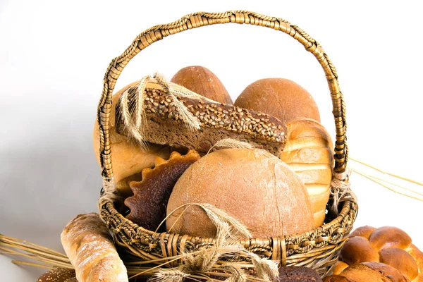 Разнообразный хлеб и сладкие булочки в корзине с шипами пшеницы на белом фоне — стоковое фото