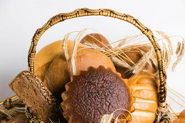 Разнообразный хлеб и сладкие булочки в корзине с шипами пшеницы на белом фоне — стоковое фото
