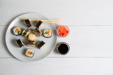 Suşi açık gri arkaplanda bir tabakta yuvarlanıyor, bambu çubuklar, soya sosu ve zencefil, düz yatış, kopyalama alanı.