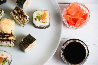 Suşi açık gri arkaplanda bir tabakta yuvarlanıyor, bambu çubuklar, soya sosu ve zencefil, düz yatış, kopyalama alanı.