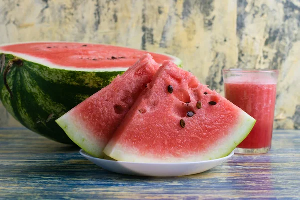 Yarı tatlı karpuz, bardakta smoothie ve mavi arka planda beyaz bir tabakta dilimlenmiş karpuz..