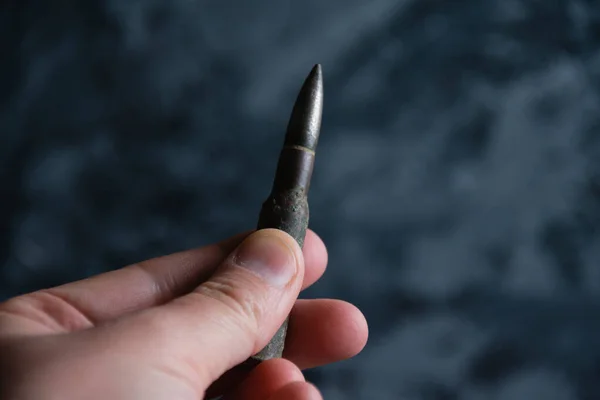 Cartridge in hand close up on dark gray concrete background, copy space. The concept of modern armaments, the war in Ukraine and the defense of the state. — Stockfoto