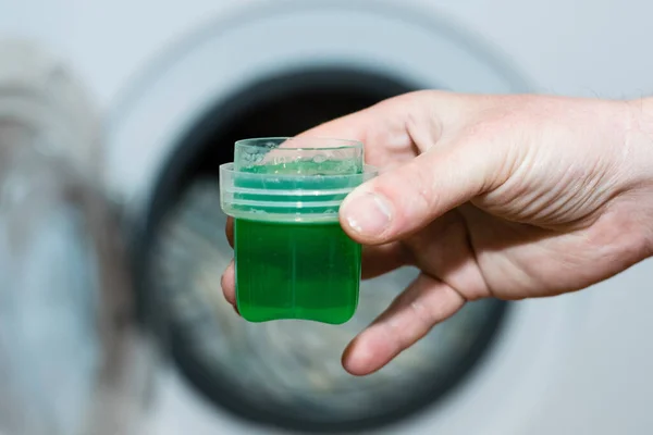 Washing gel close up in male hand on the background of the washing machine with linen.