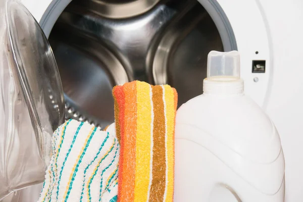 Bottle with washing gel and colorful towels near the washing machine.