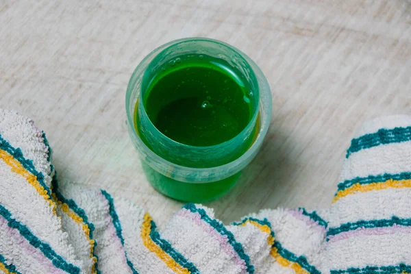 透明ディスペンサーで緑色を洗浄するための液体ゲルと明るい木製の背景に着色タオル — ストック写真