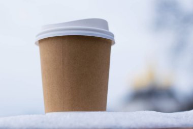 Kahverengi kağıt bardakta kahve. Kışın sokakta şehrin ve parkın arka planına karşı..