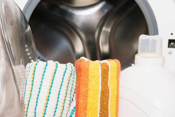 Bottle with washing gel and colorful towels near the washing machine.