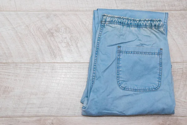 Men\'s denim pants in blue on a light wooden background.