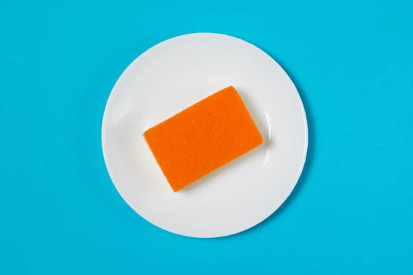 Πορτοκαλί Πορώδες Σφουγγάρι Για Πλύσιμο Πιάτων Λευκό Πιάτο Μπλε Φόντο — Φωτογραφία Αρχείου