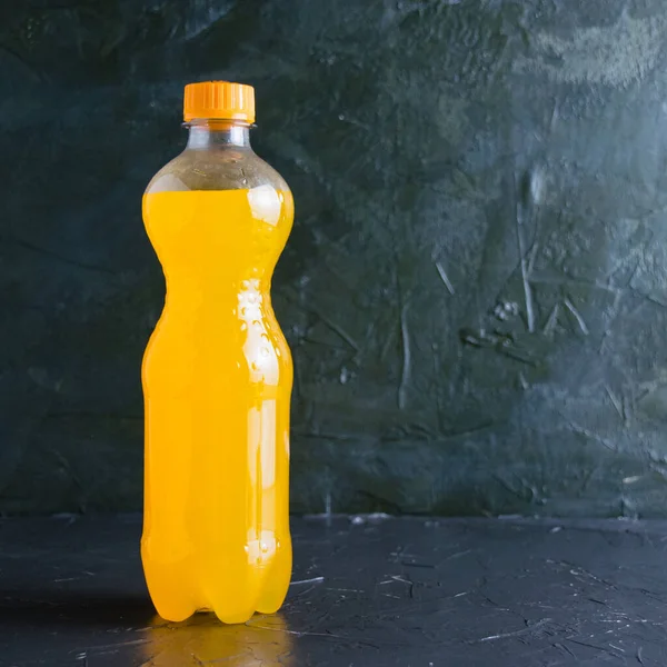 Yellow carbonated drink in a plastic bottle on a dark gray background with copy space.
