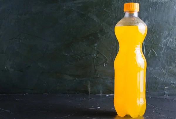 Yellow carbonated drink in a plastic bottle on a dark gray background with copy space.