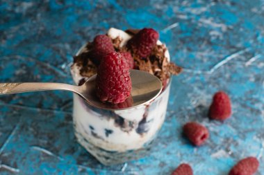 Bir adam lezzetli bir tatlıyı ahududu, yoğurt, yulaf ezmesi ve çikolatayla yer. Kaşıkla yakın plan tatlı..