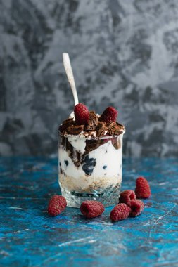 Bir adam lezzetli bir tatlıyı ahududu, yoğurt, yulaf ezmesi ve çikolatayla yer. Kaşıkla yakın plan tatlı..