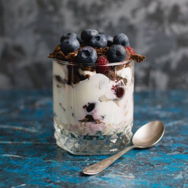 Çikolatalı, yoğurtlu, yaban mersinli ve ahududulu tatlı ve arka planda fotokopi alanı olan bir kaşık..
