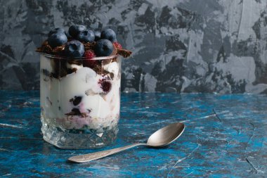 Çikolatalı, yoğurtlu, yaban mersinli ve ahududulu tatlı ve arka planda fotokopi alanı olan bir kaşık..