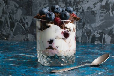 Çikolatalı, yoğurtlu, yaban mersinli ve ahududulu tatlı ve arka planda fotokopi alanı olan bir kaşık..