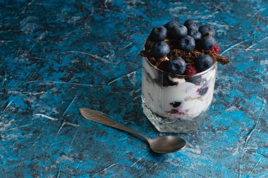 Çikolatalı, yoğurtlu, yaban mersinli ve ahududulu tatlı ve arka planda fotokopi alanı olan bir kaşık..