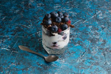 Çikolatalı, yoğurtlu, yaban mersinli ve ahududulu tatlı ve arka planda fotokopi alanı olan bir kaşık..