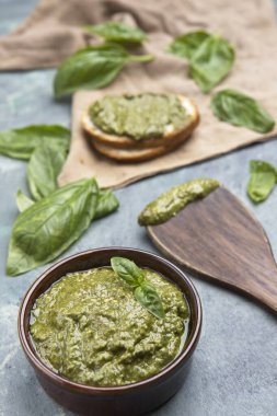 Arka planda ahşap spatula, ekmek ve fesleğen yapraklı ev yapımı pesto sosu resmi.
