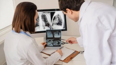 Genç doktorların geçmişe bakış radyologları röntgen ve bilgisayar tomografisi filmlerini analiz eder ve defterde tıbbi bir açıklama yapar.